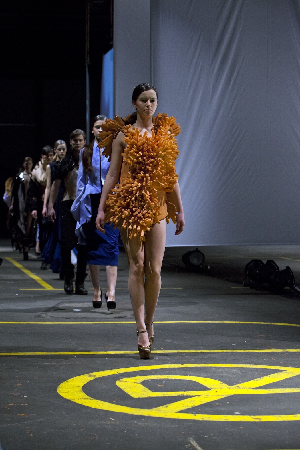 Fashion models walking in a line in an industrial hall with white sails in the background