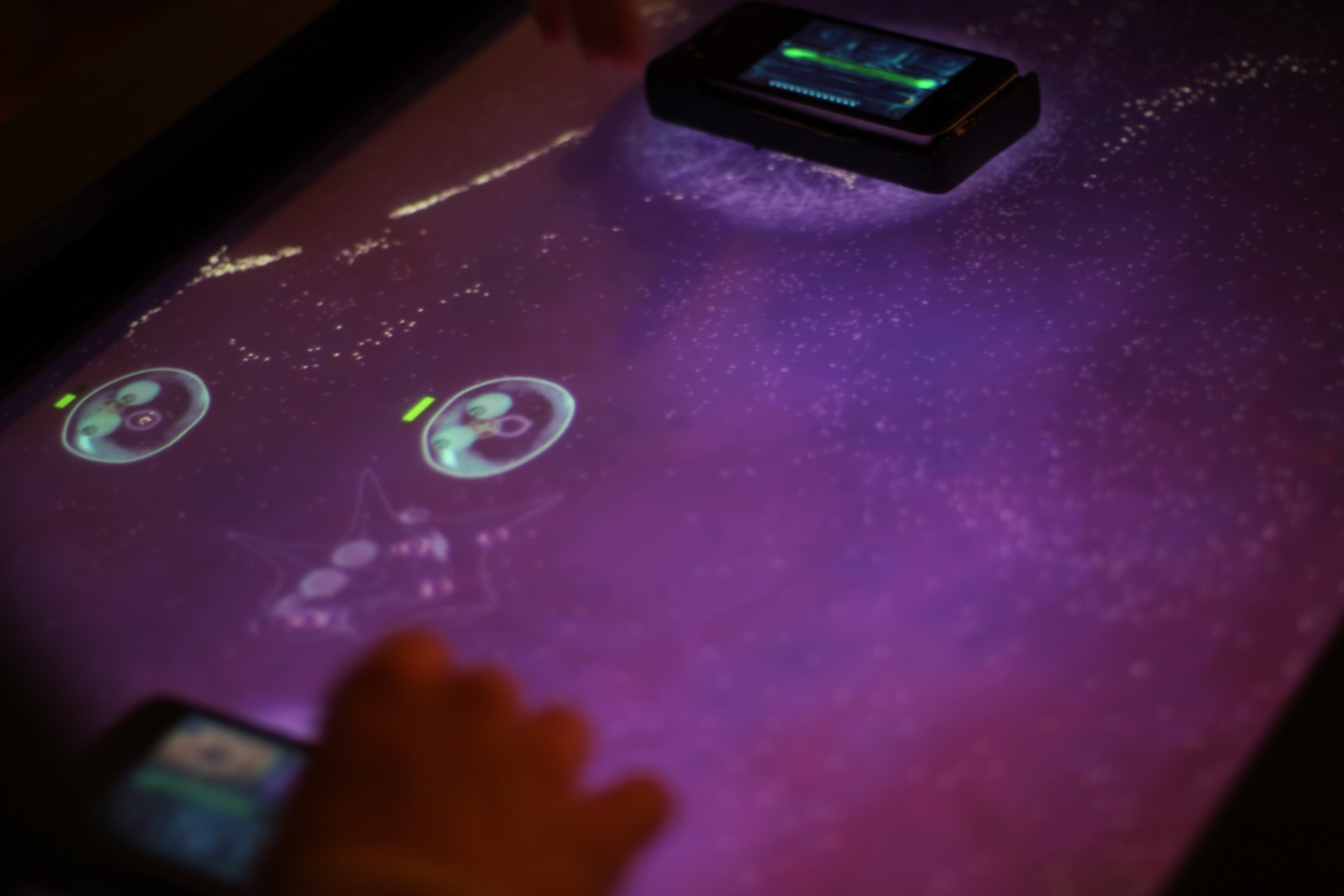 Hands moving iPhones over a multitouch surface displaying animated cells