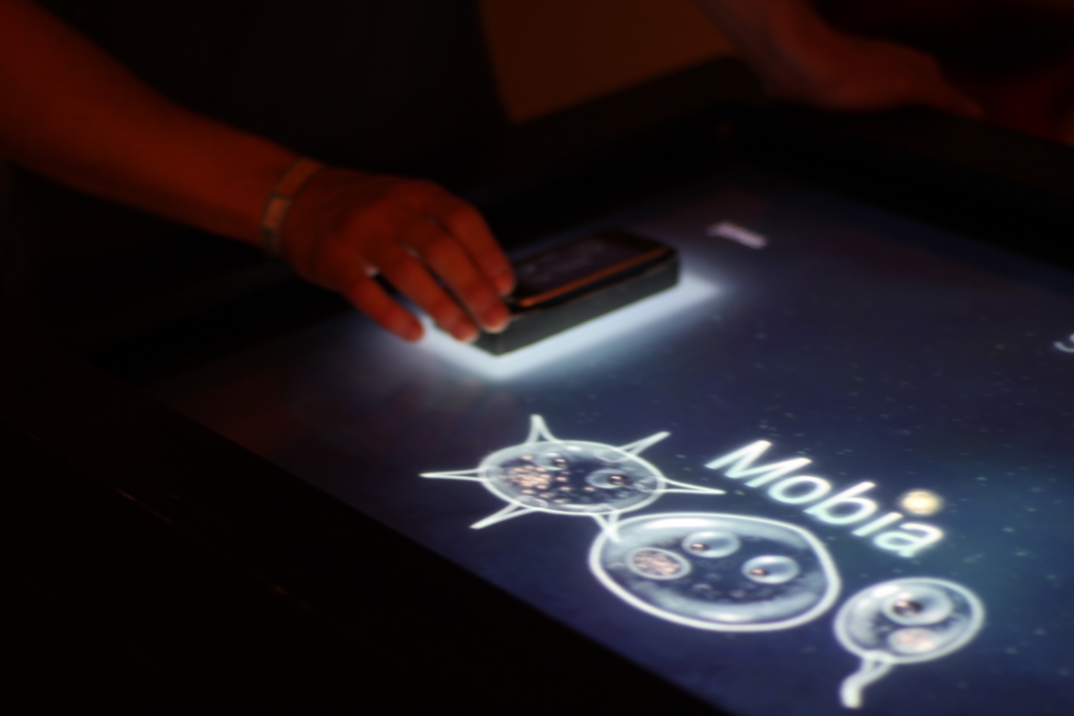 Hands moving iPhones over a multitouch surface displaying animated cells